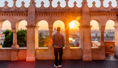 Man die tussen de bogen staat en bij zonsopgang vanaf het Vissersbastion uitkijkt over het stadsgezicht van Boedapest, Hongarije