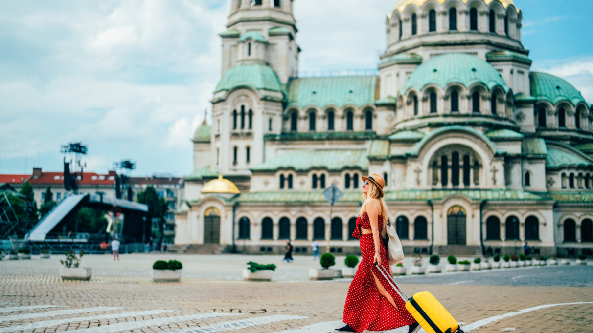Een individuele reiziger loopt met een gele koffer over het plein voor de Alexander Nevski-kathedraal in Sofia, Bulgarije. Een jonge toerist verkent de stad, geniet van culturele bezienswaardigheden en ontdekt iconische Europese monumenten tijdens een zomervakantie.