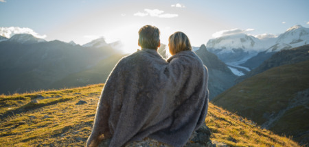 Een stel zit dicht tegen elkaar aan onder een deken en kijkt naar de zonsopgang boven de bergen in Zwitserland