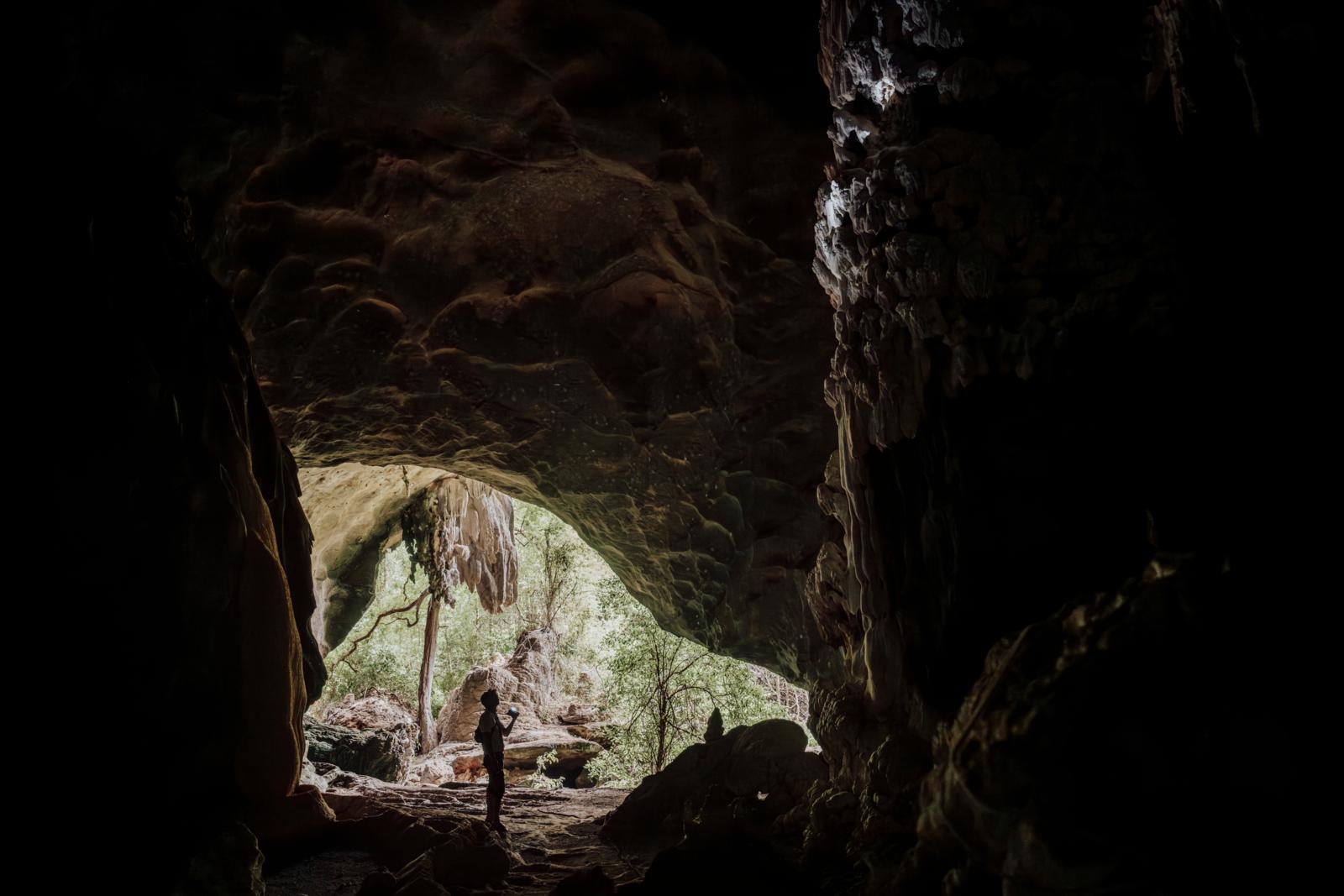 Reiziger kijkt uit op het daglicht bij de ingang van een kalksteengrot in Had Chao Mai National Park in Thailand