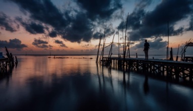 Reiziger op een houten steiger aan het water tijdens een dramatische zonsondergang in Nakhon Si Thammarat, Thailand
