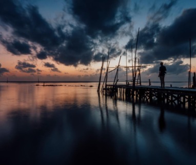 Reiziger op een houten steiger aan het water tijdens een dramatische zonsondergang in Nakhon Si Thammarat, Thailand