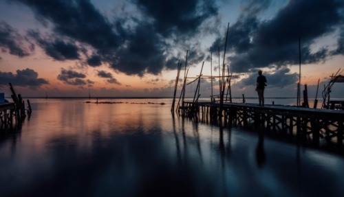 Reiziger op een houten steiger aan het water tijdens een dramatische zonsondergang in Nakhon Si Thammarat, Thailand
