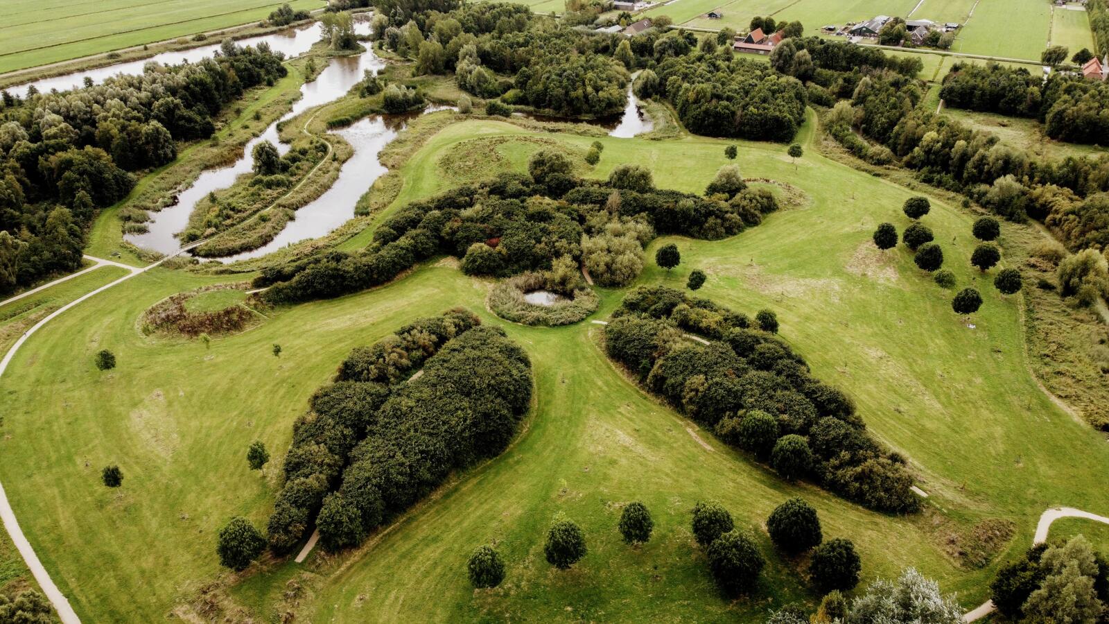 Een prachtige luchtfoto van Landart kunstwerk Moeder Aarde in het Abtswoudse bos, een landschapskunstwerk in de vorm van een liggende vrouw omringd door groen en water.