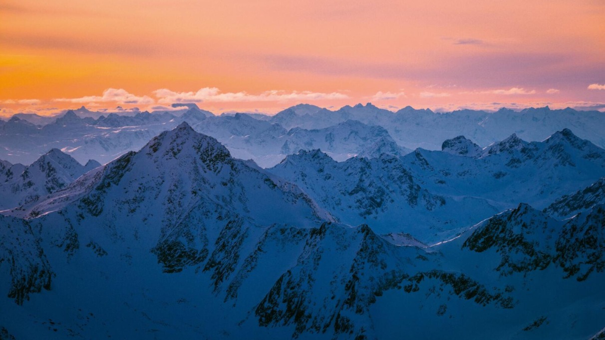 Besneeuwde bergtoppen in Tirol bij een oranje en roze zonsondergang