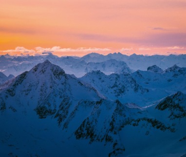 Besneeuwde bergtoppen in Tirol bij een oranje en roze zonsondergang