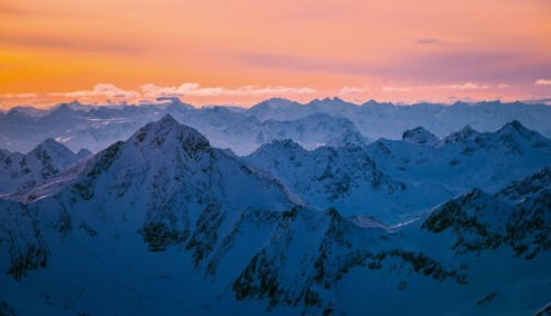 Besneeuwde bergtoppen in Tirol bij een oranje en roze zonsondergang