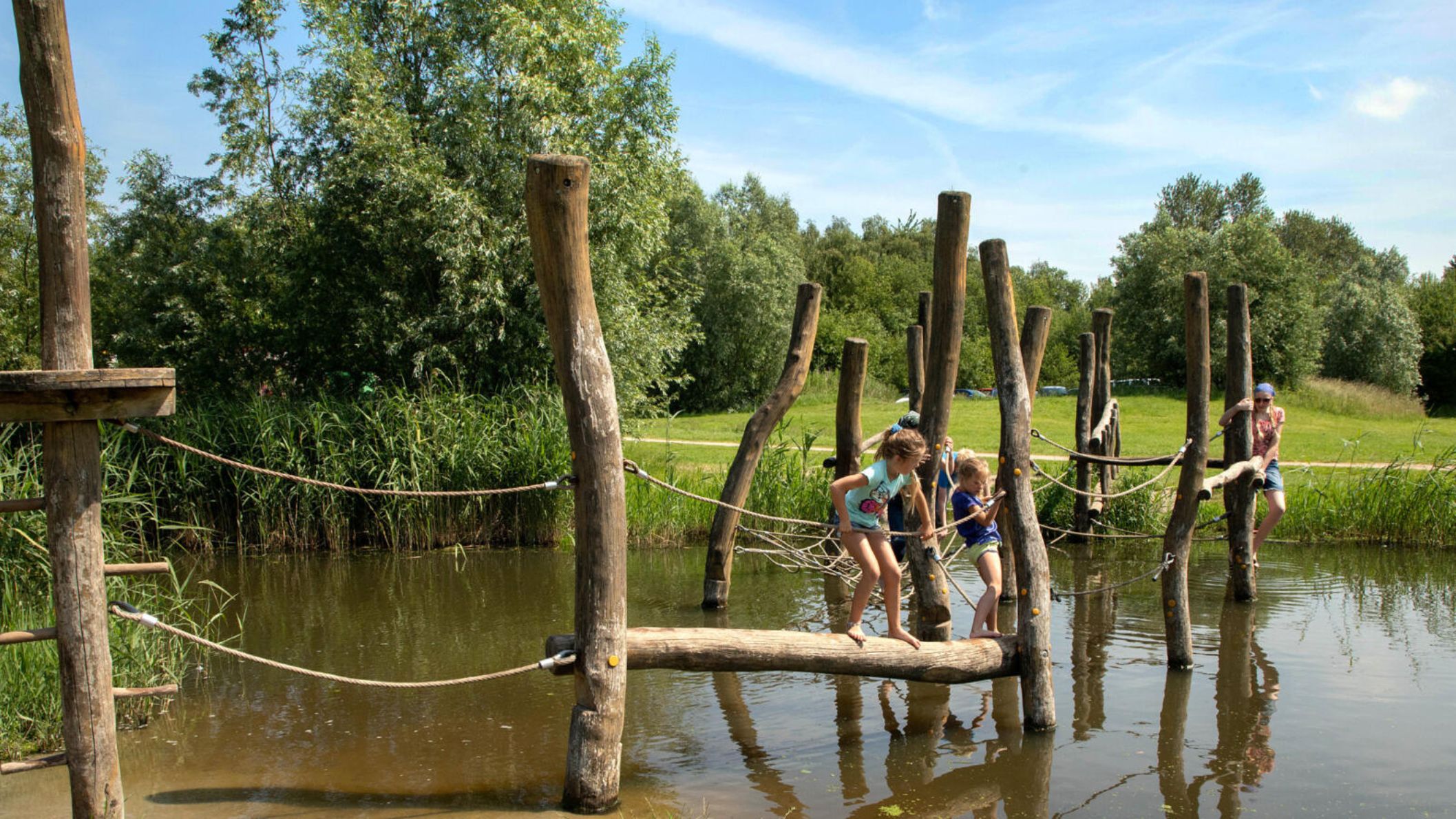 Kinderen balanceren over houten boomstammen en touwen van een survivalparcours boven het water in Het Belevenissenbos bij Lelystad.