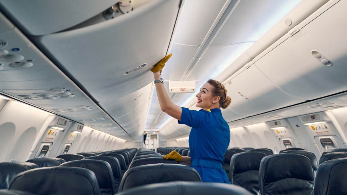 Zijaanzicht van een vrolijke, schattige stewardess in uniform die het opbergvak in de vliegtuigcabine sluit