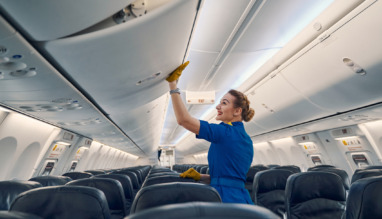 Zijaanzicht van een vrolijke, schattige stewardess in uniform die het opbergvak in de vliegtuigcabine sluit