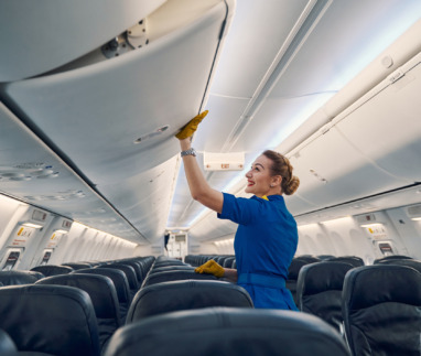 Zijaanzicht van een vrolijke, schattige stewardess in uniform die het opbergvak in de vliegtuigcabine sluit
