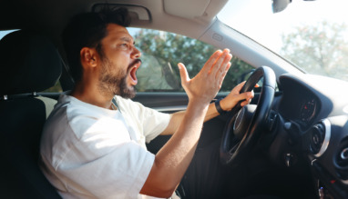 Een boze, schreeuwende man achter het stuur van een auto.