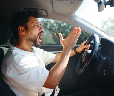 Een boze, schreeuwende man achter het stuur van een auto.