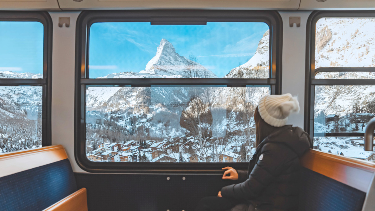 Een vrolijke toeriste die vanuit de trein uit het raam kijkt en geniet van de besneeuwde Matterhorn, in Zermatt in Zwitserland.