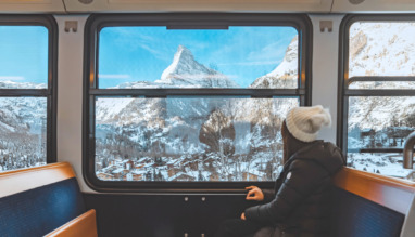 Een vrolijke toeriste die vanuit de trein uit het raam kijkt en geniet van de besneeuwde Matterhorn, in Zermatt in Zwitserland.