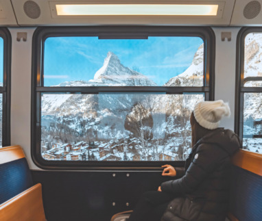 Een vrolijke toeriste die vanuit de trein uit het raam kijkt en geniet van de besneeuwde Matterhorn, in Zermatt in Zwitserland.