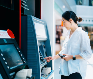 Jonge Aziatische vrouw die een geldautomaat (ATM) gebruikt in een winkelcentrum. Geld opnemen, rekeningen betalen, het saldo controleren en een overschrijving doen. Persoonlijk bankieren. Bescherming van de privacy. Beveiliging van mobiel bankieren. Zelfbedieningsconcept