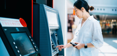 Jonge Aziatische vrouw die een geldautomaat (ATM) gebruikt in een winkelcentrum. Geld opnemen, rekeningen betalen, het saldo controleren en een overschrijving doen. Persoonlijk bankieren. Bescherming van de privacy. Beveiliging van mobiel bankieren. Zelfbedieningsconcept