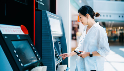 Jonge Aziatische vrouw die een geldautomaat (ATM) gebruikt in een winkelcentrum. Geld opnemen, rekeningen betalen, het saldo controleren en een overschrijving doen. Persoonlijk bankieren. Bescherming van de privacy. Beveiliging van mobiel bankieren. Zelfbedieningsconcept