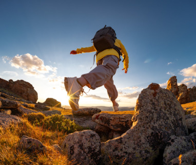 Een vrouwelijke wandelaar springt of zet grote stappen van rots naar rots op de bergtop bij zonsondergang.