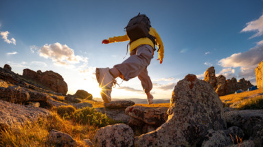 Een vrouwelijke wandelaar springt of zet grote stappen van rots naar rots op de bergtop bij zonsondergang.