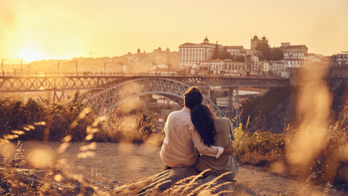 Een verliefd stel zit bij zonsondergang voor de Dom Luis-brug, Porto, Portugal