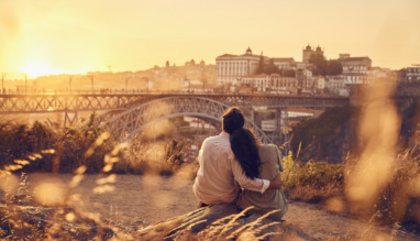 Een verliefd stel zit bij zonsondergang voor de Dom Luis-brug, Porto, Portugal