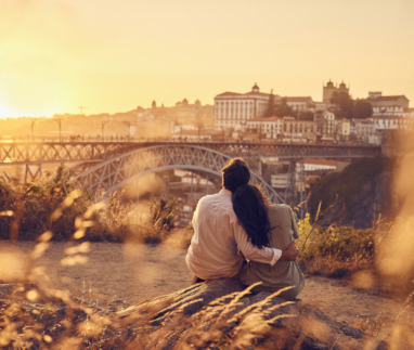 Een verliefd stel zit bij zonsondergang voor de Dom Luis-brug, Porto, Portugal
