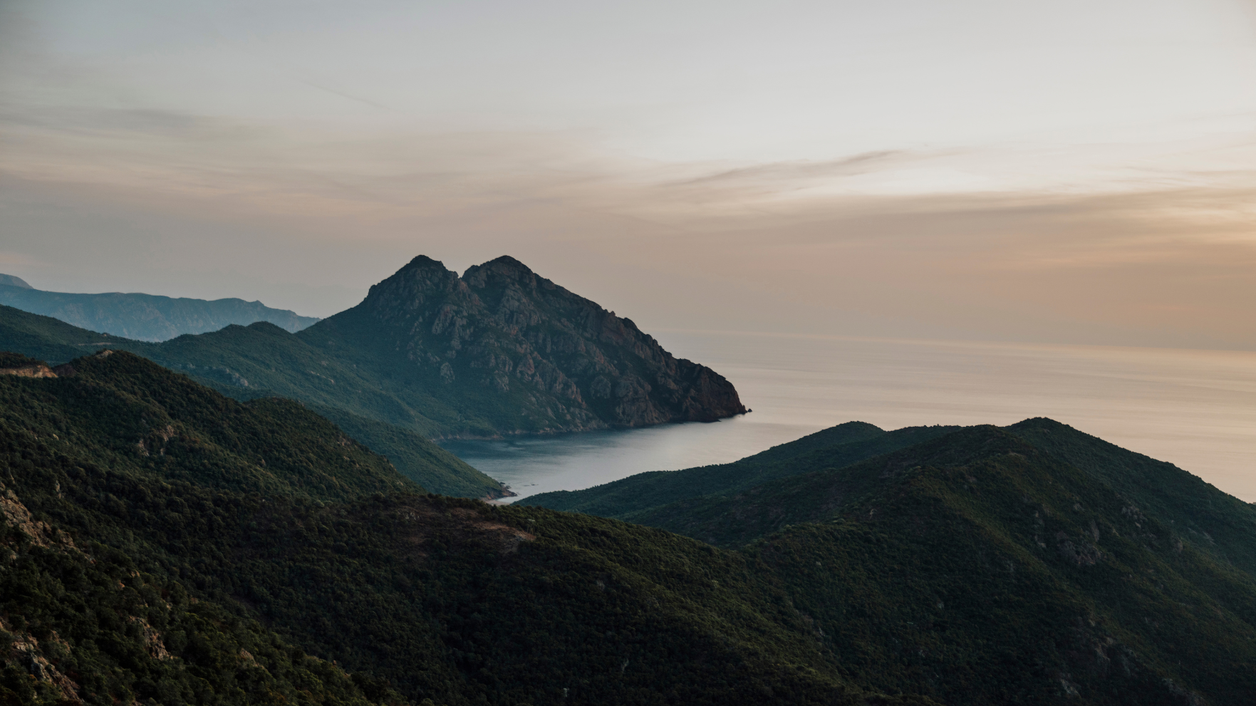 Panoramisch uitzicht over groene bergen, steile rotsen en de Middellandse Zee op Corsica bij zonsondergang