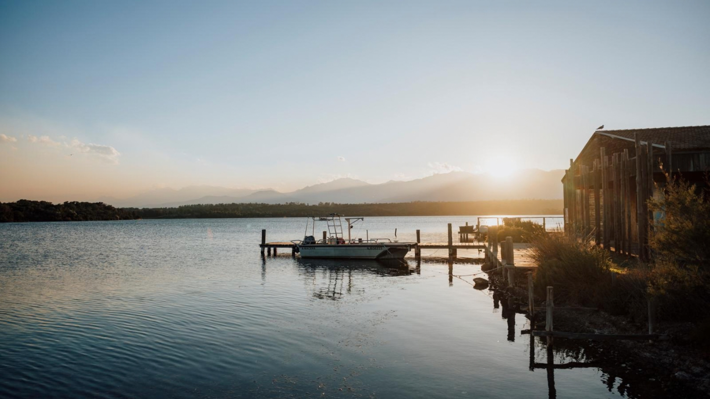 Bootje aan een houten steiger bij een houten hut op het water van Étang d’Urbino bij zonsondergang op Corsica