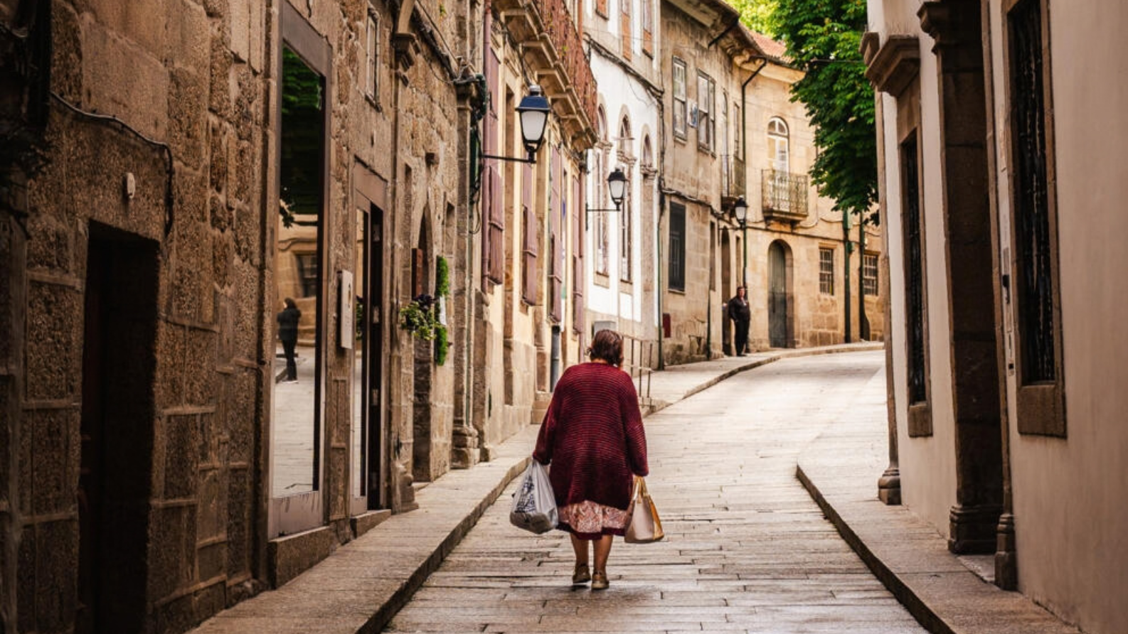Een vrouw met boodschappentassen loopt door een smalle, geplaveide straat in het historische centrum van Guimarães