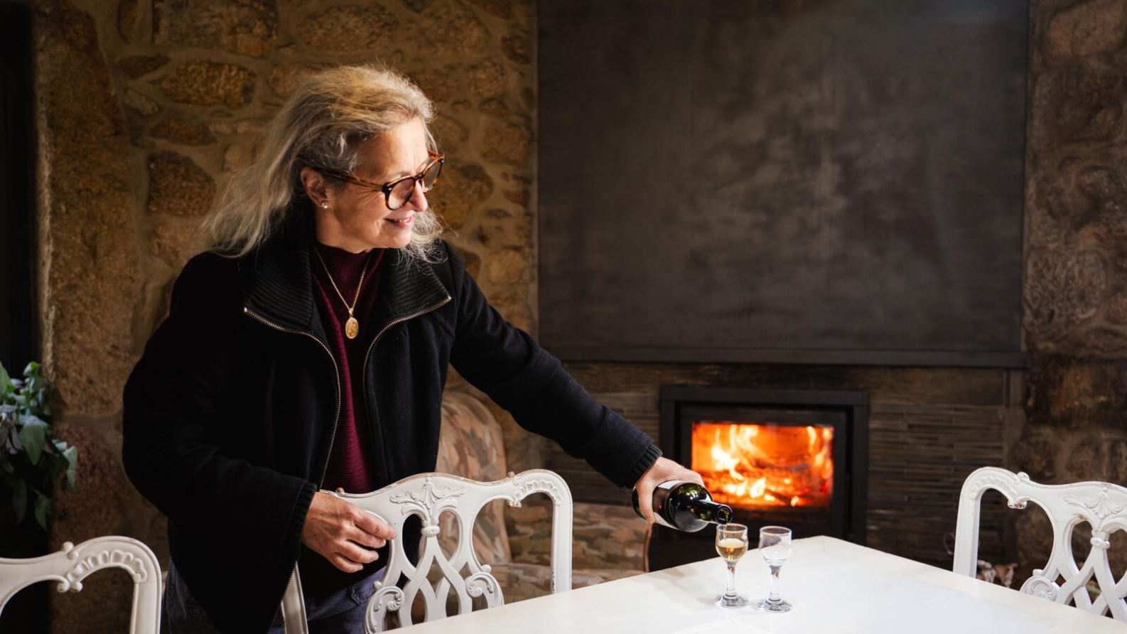 Vrouw schenkt een drankje in voor een brandende open haard bij Trebid'Ouro