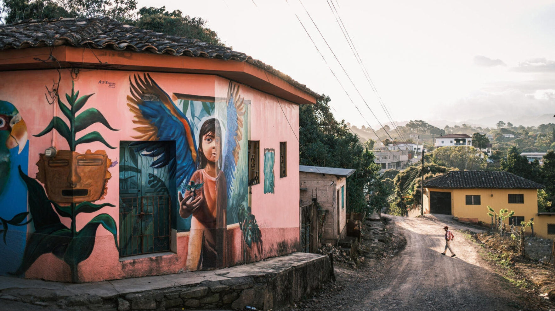 Kleurrijk roze huis met muurschilderingen langs een onverharde weg in Dulce Nombre, Honduras