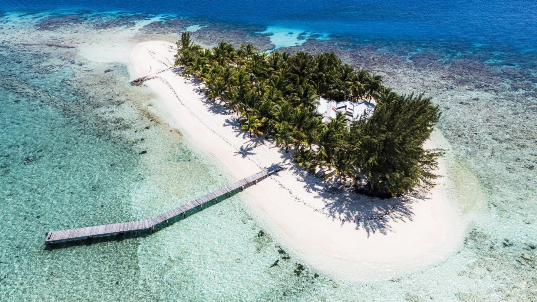 Luchtfoto van een tropisch eiland met palmbomen, zandstrand en een steiger bij Utila, Honduras