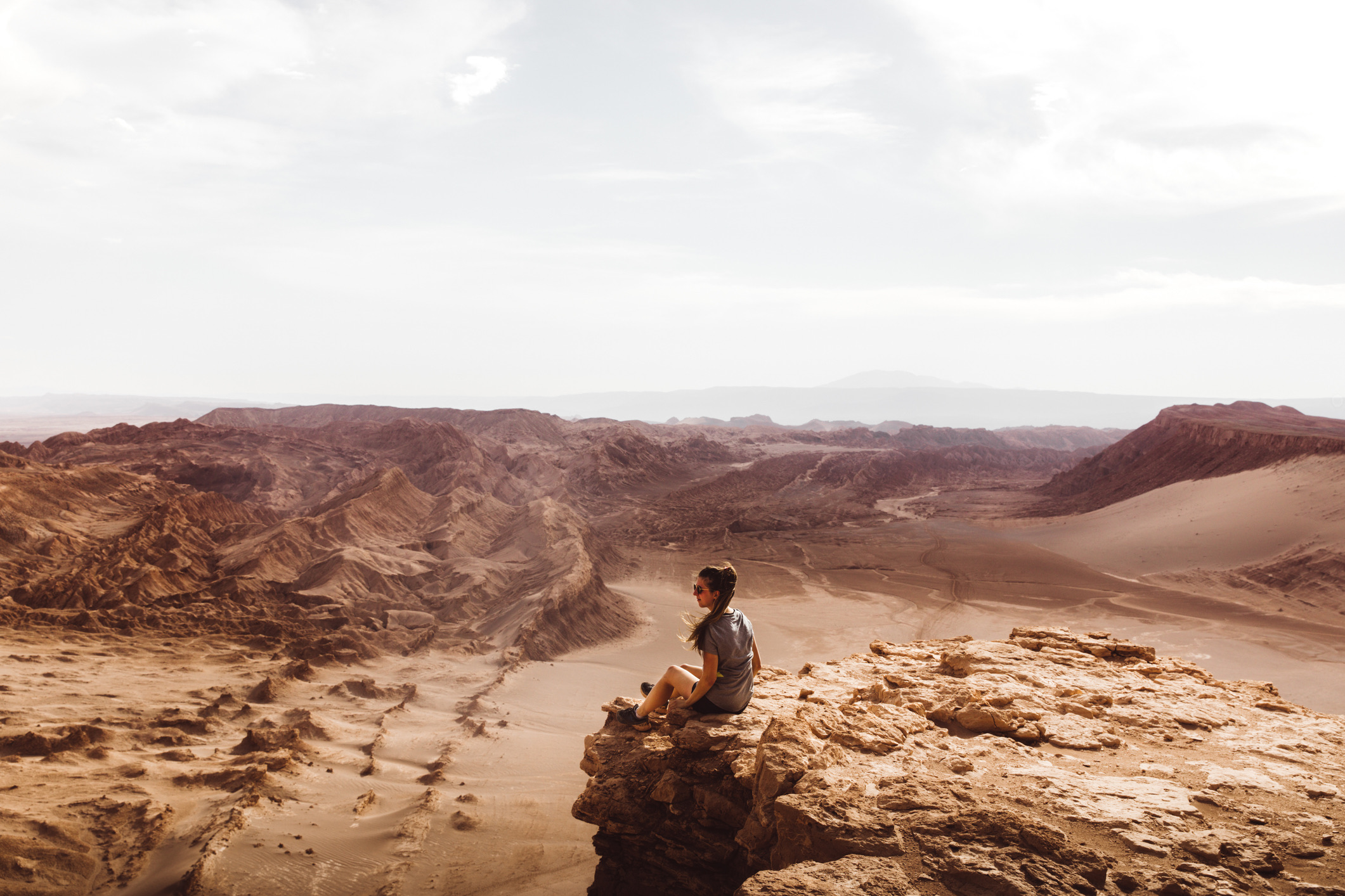 Silhouet van een jonge vrouw die aan de rand van de klif staat en tijdens de zonsondergang uitkijkt over het woestijnlandschap in de Atacama-regio, Chili
