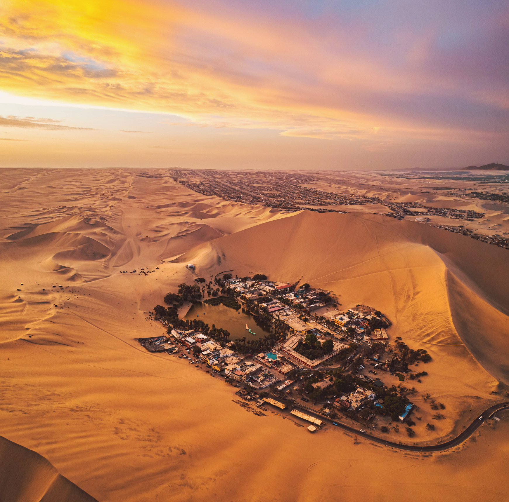 De gouden oase van Huacachina ligt verscholen tussen hoge zandduinen, met de uitgestrekte horizon onder een prachtige zonsonderganghemel. Peru.
