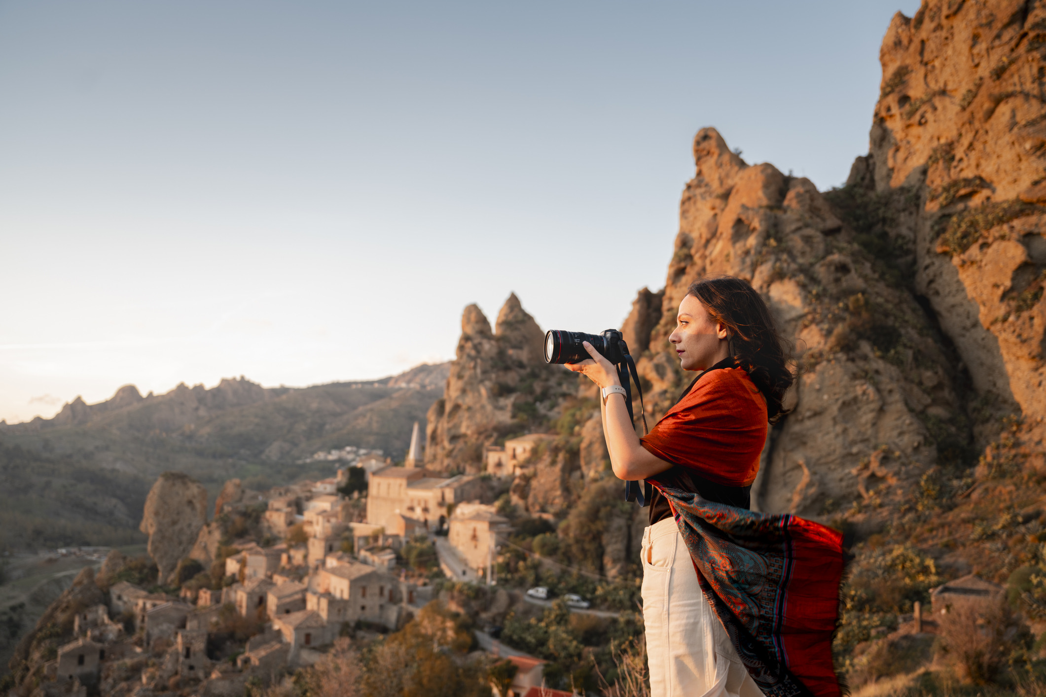 Vrouw in kleurrijke kleding die tijdens zonsondergang een schilderachtig bergdorpje fotografeert, Calabrië, Italië