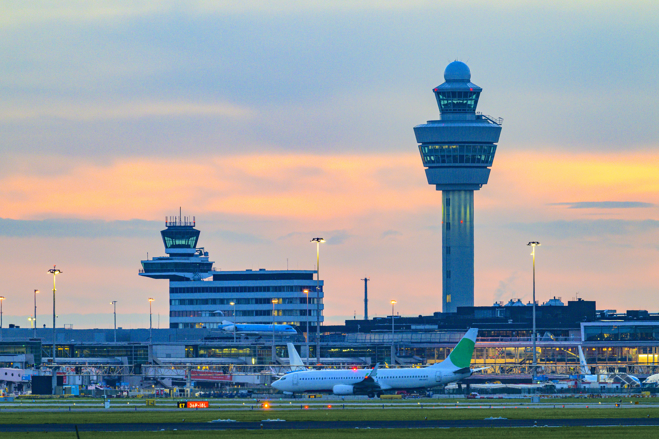 De luchthaven Schiphol met diverse vliegtuigen bij nacht. Schiphol is een van de drukste en grootste luchthavens van Europa en ligt in de buurt van Amsterdam, Nederland. Het fungeert als een belangrijk knooppunt voor internationale vluchten en is een belangrijke toegangspoort tot Europa.