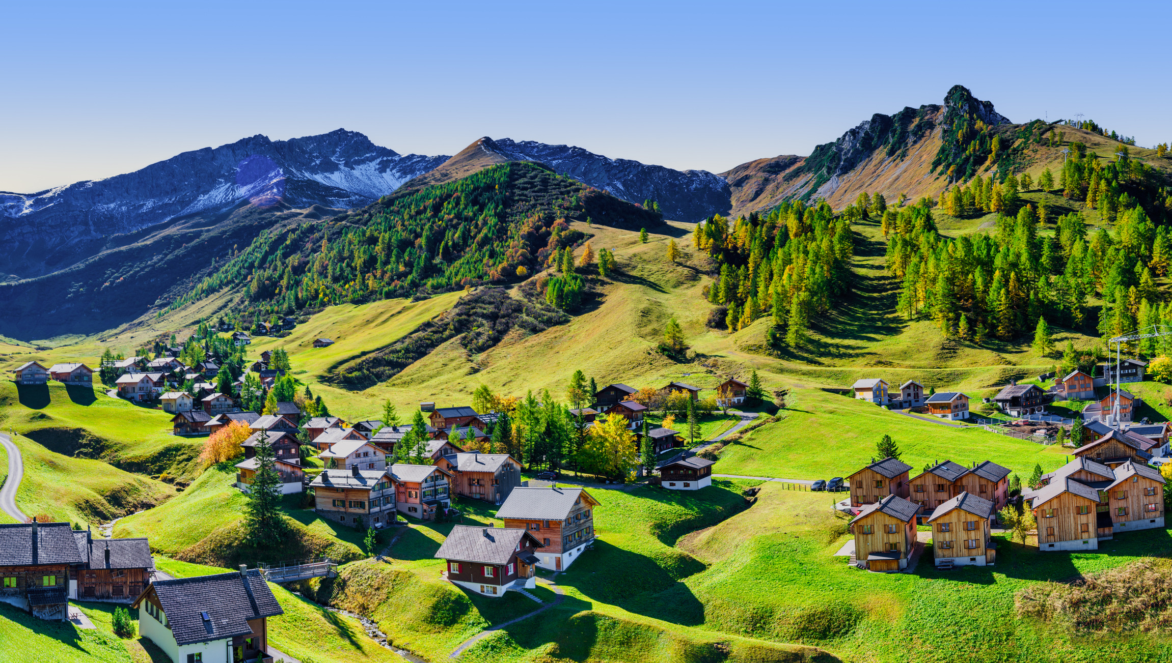 Weids panoramisch uitzicht op traditionele houten chalets, verspreid over de glooiende groene weiden van het dorp Malbun in Liechtenstein.