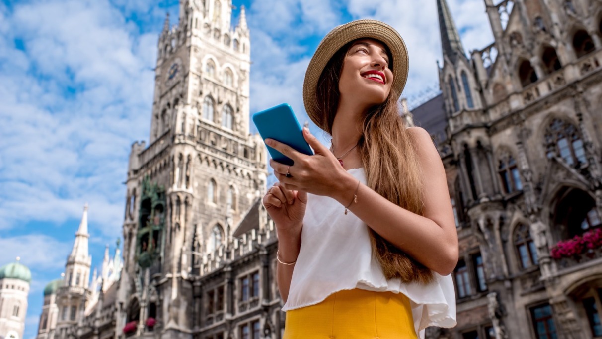 Een jonge toeriste die haar mobiele telefoon gebruikt op het centrale plein voor het beroemde stadhuis in München