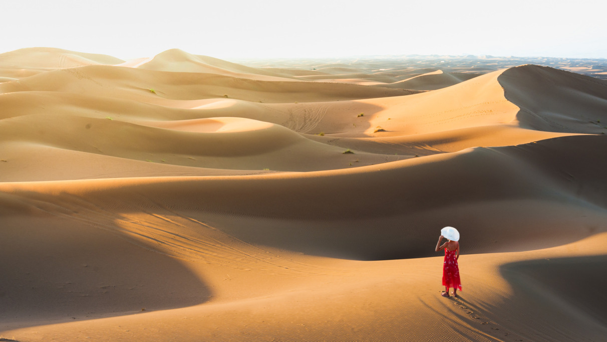 Een vrouw in een elegante jurk die geniet van het uitzicht vanaf een zandduin in de Sahara, Marokko, Noord-Afrika.