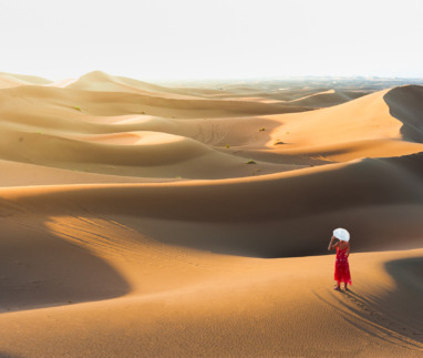 Een vrouw in een elegante jurk die geniet van het uitzicht vanaf een zandduin in de Sahara, Marokko, Noord-Afrika.