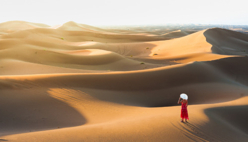 Een vrouw in een elegante jurk die geniet van het uitzicht vanaf een zandduin in de Sahara, Marokko, Noord-Afrika.