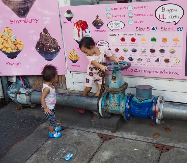 Spelende kinderen in Bangkok. Tegen de achtergrond van een ijsjesposter kun je denken dat ze hopen dat er ijs in de buis zit.