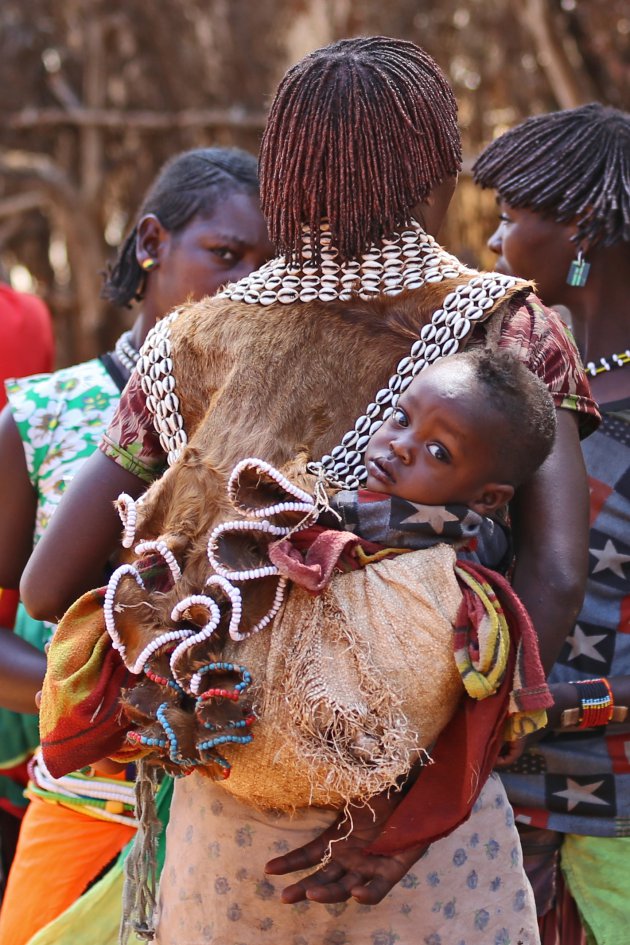 Baby van de Bana stam op de rug van haar moeder op de markt in Key Afar