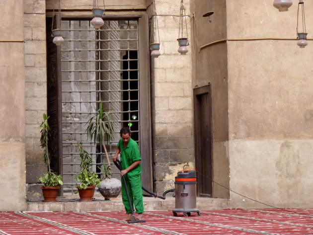 Deze man stofzuigt het tapijt in de Sultan Hassan moskee