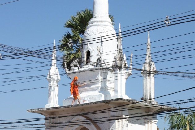 Monnik schildert tempel in Pakse achter elektriciteitsdraden