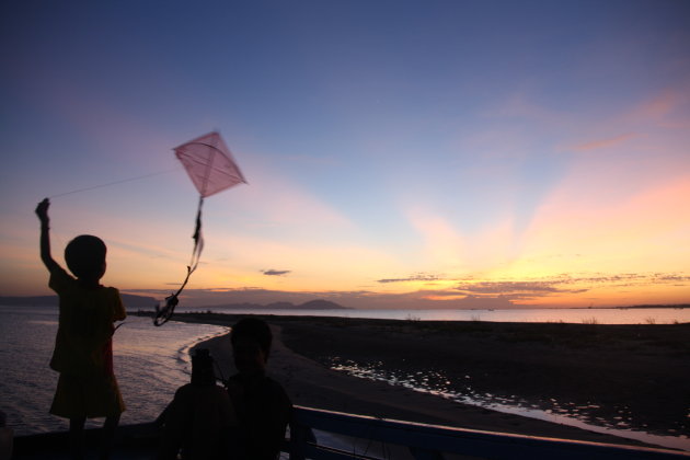 Kindje met vlieger op de boot tijdens zonsondergang bij Kampot