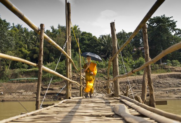 Monnik loopt op de brug over de Mekong.
