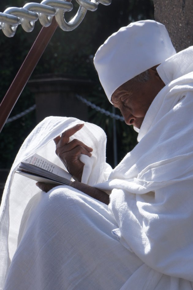 met zijn kleding schaduw zoekend zat deze geestelijke te bidden voor de kathedraal in Addis